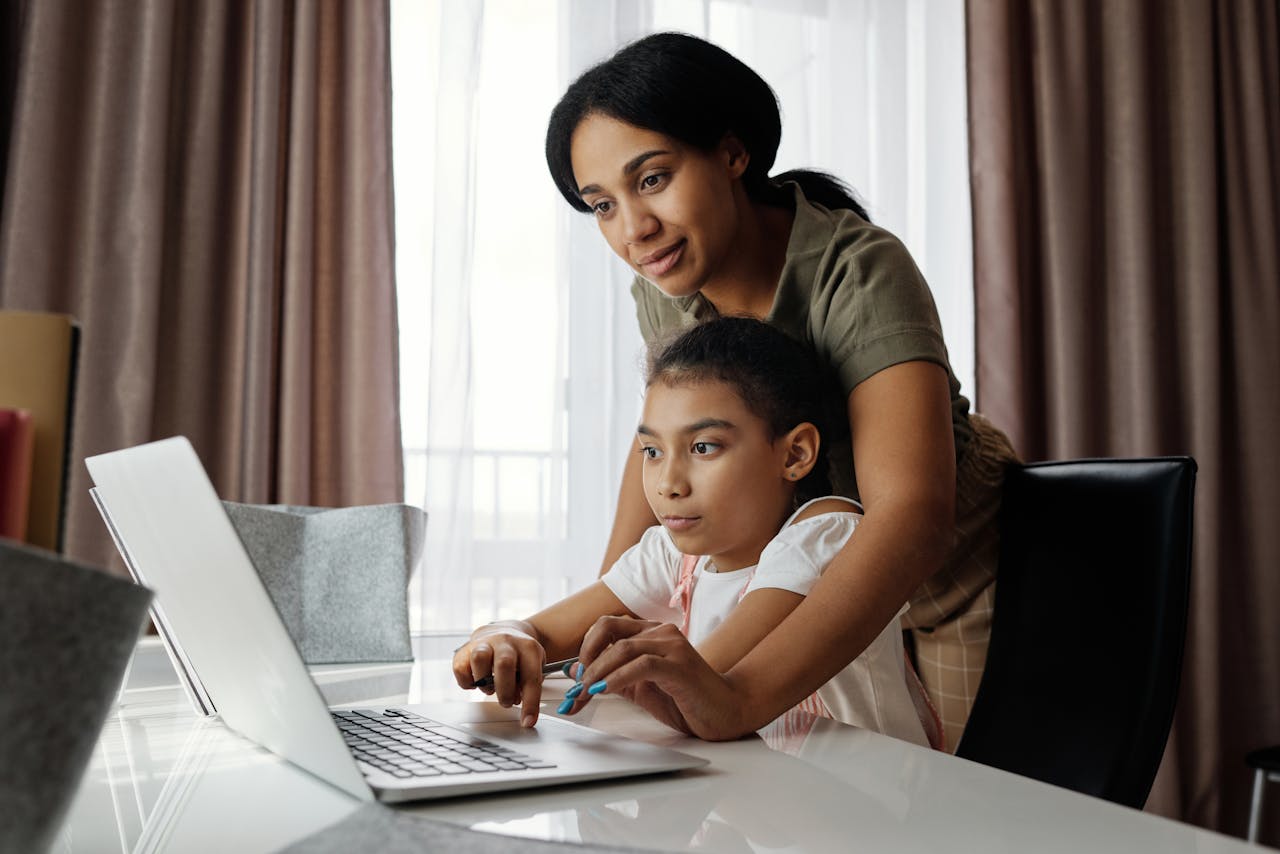 services-01 A mother helps her daughter with an online lesson on a laptop, showcasing family bonding and education at home.