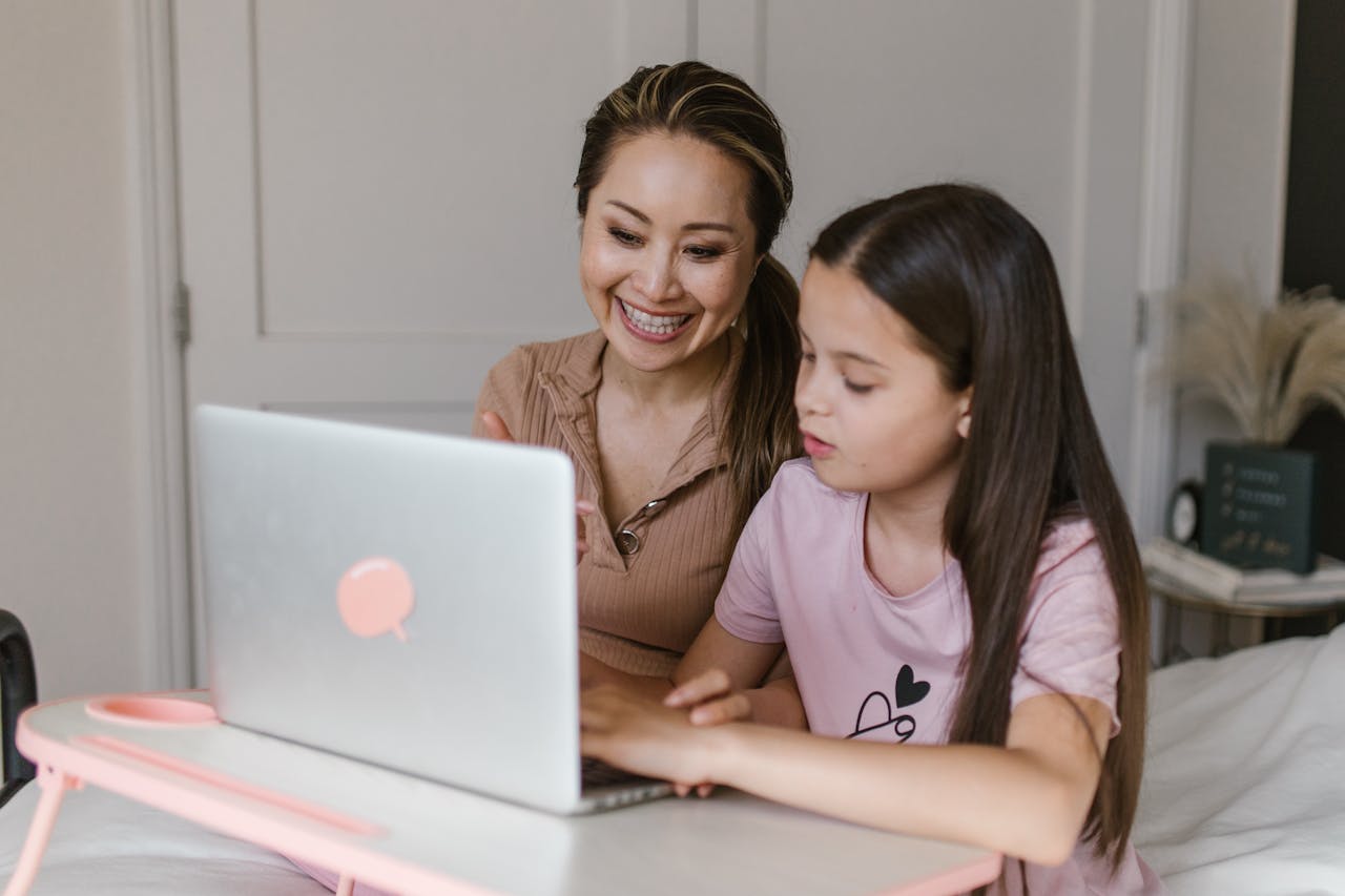 who-we-are A mother and daughter smile and learn together using a laptop at home.